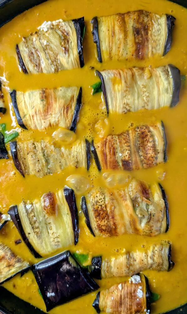 A pan of rolled aubergine slices in a saffron-yellow sauce