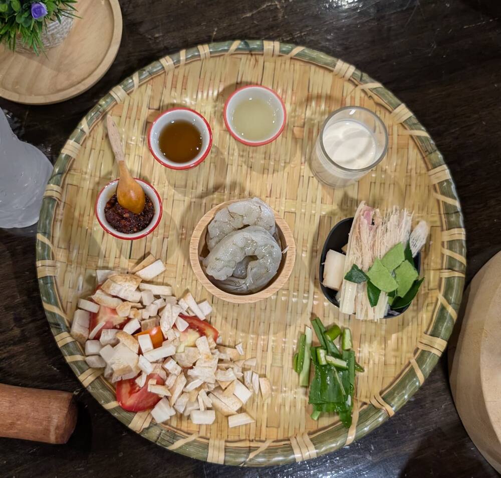 A woven basket set out with prawns, tofu, spring onions, chilli and dipping sauces, ready to cook