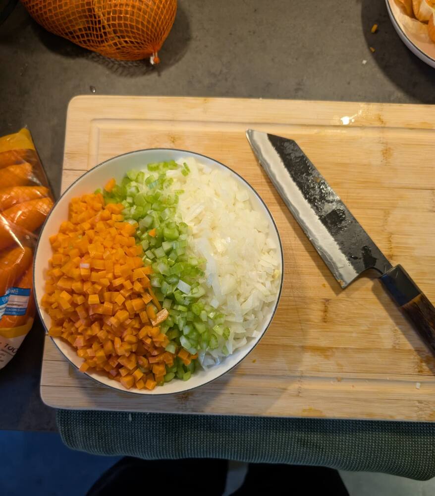 Diced carrot, celery and onion in a bowl on a wooden board, a Japanese knife alongside