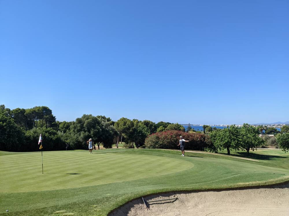 Two players on a green by the sea under a cloudless sky