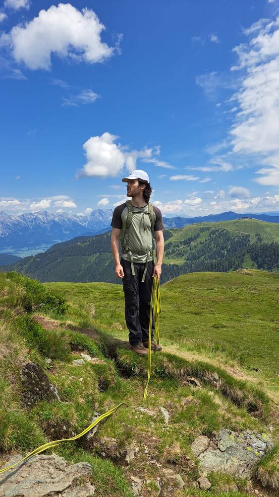 Standing on a grassy ridge path in summer, snow-capped peaks and a lake far below