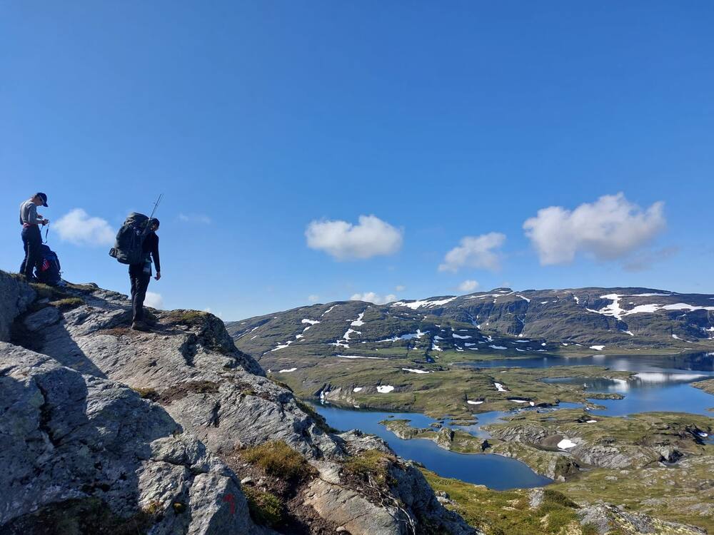 Two hikers with packs on a rocky crest above a plateau of lakes and snowfields